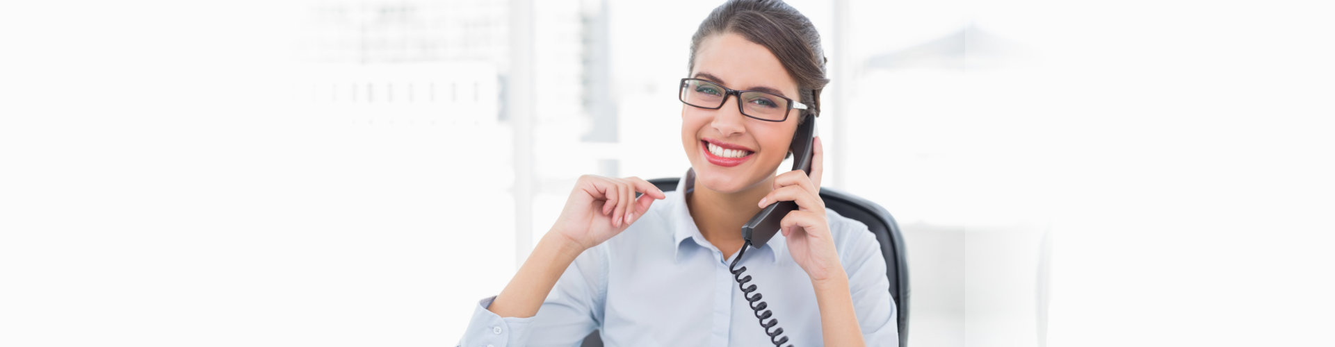 Delighted classy brown haired businesswoman answering the telephone in bright office