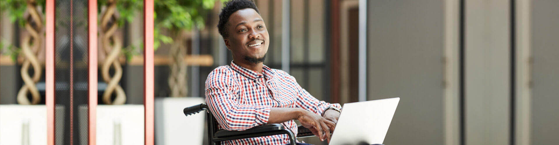 African smiling man sitting in wheelchair and using laptop computer in the mall